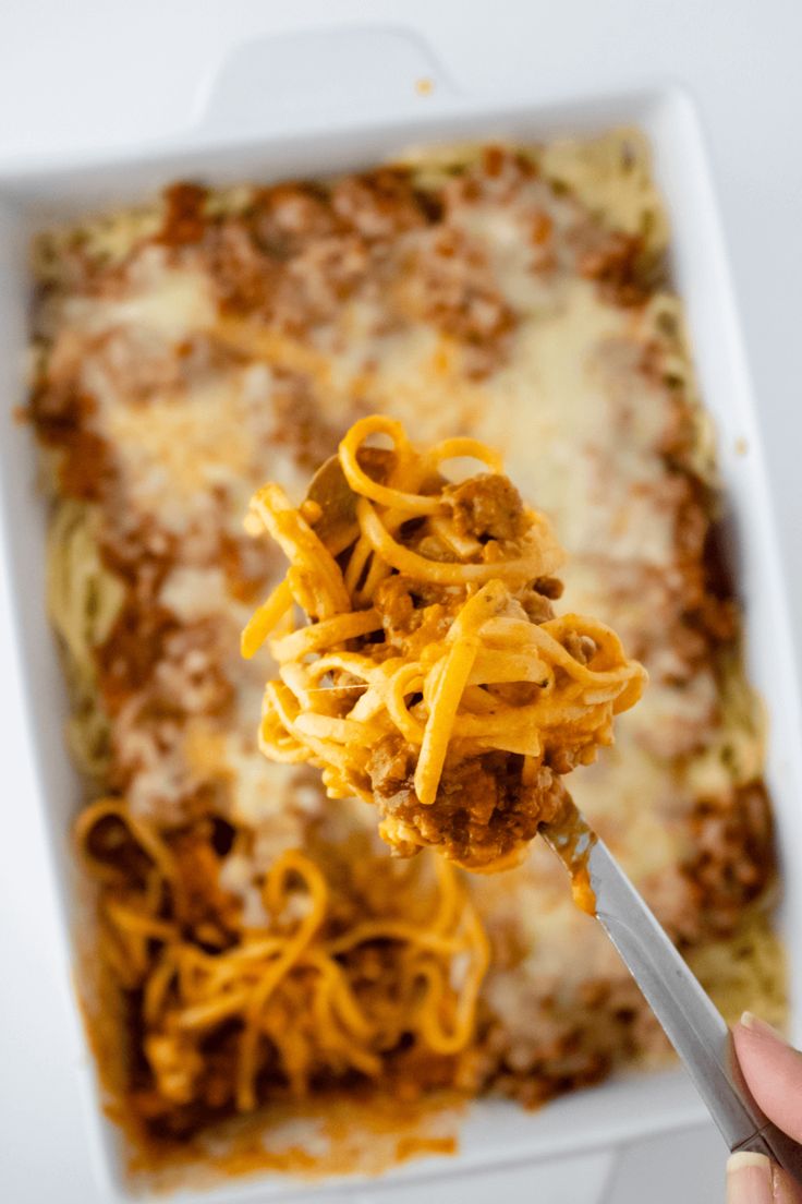 a person holding a spoon full of spaghetti in a casserole dish with meat and cheese