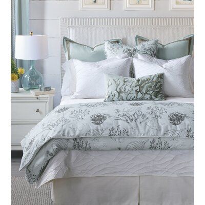 a bed with white and blue comforters in a bedroom next to a lamp on a dresser