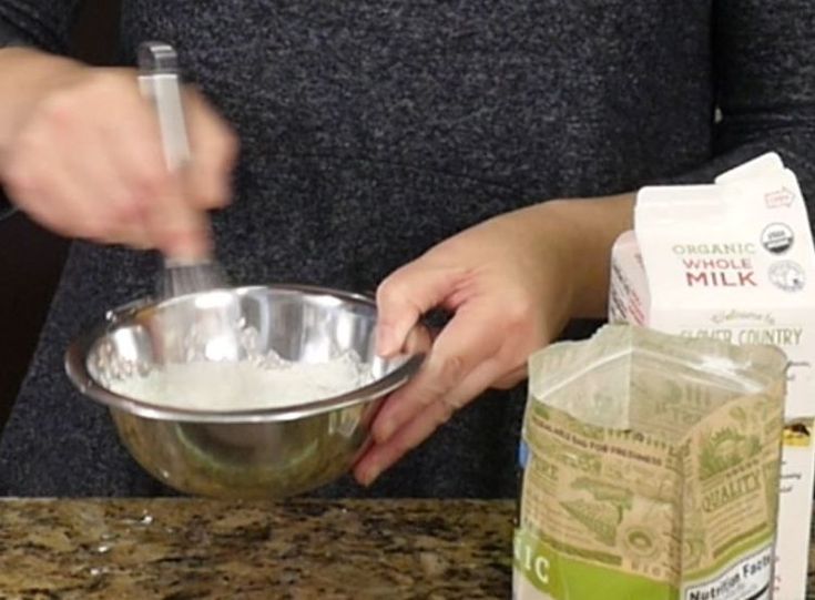 a person mixing something in a bowl on top of a counter next to bags of milk