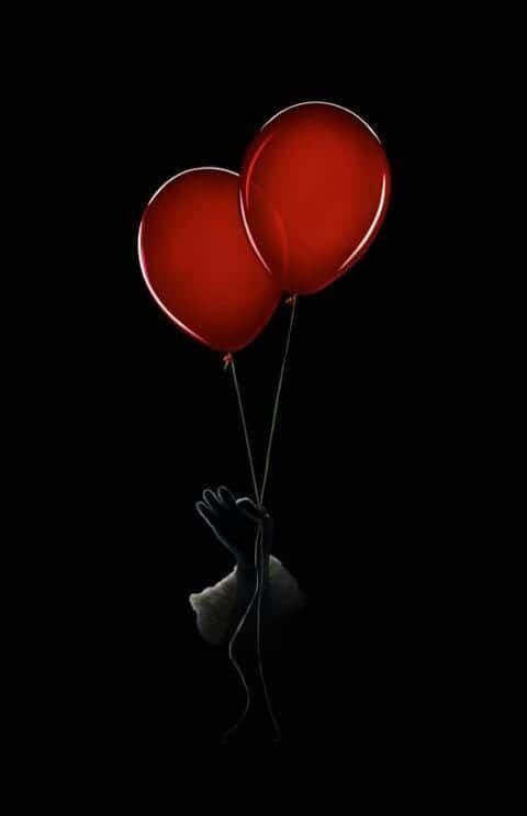 two red balloons floating in the air with a person holding them up to their face