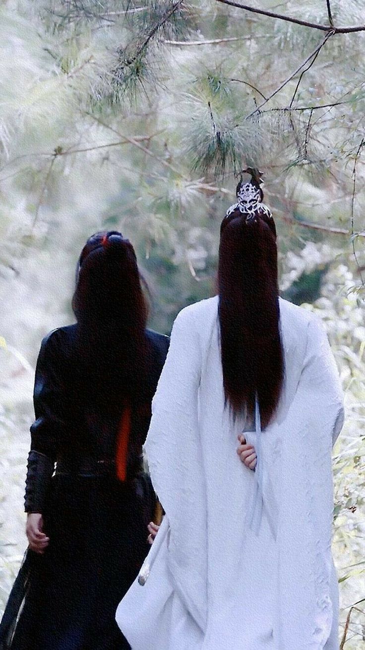 two women dressed in black and white are walking through the woods with long dark hair