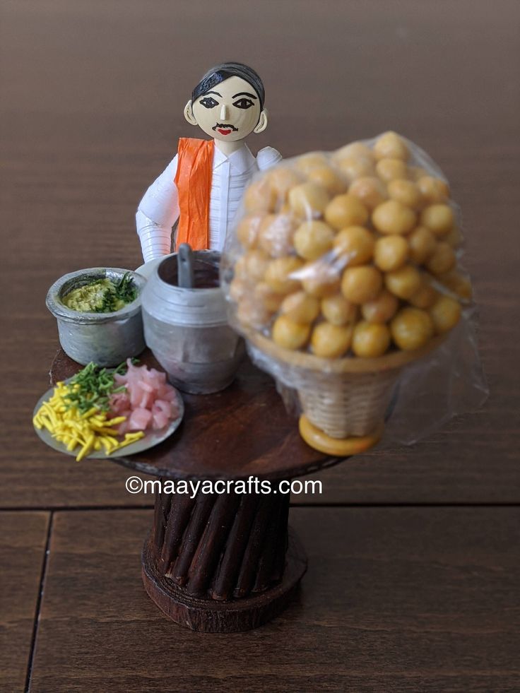 a doll sitting on top of a wooden table next to a basket filled with food