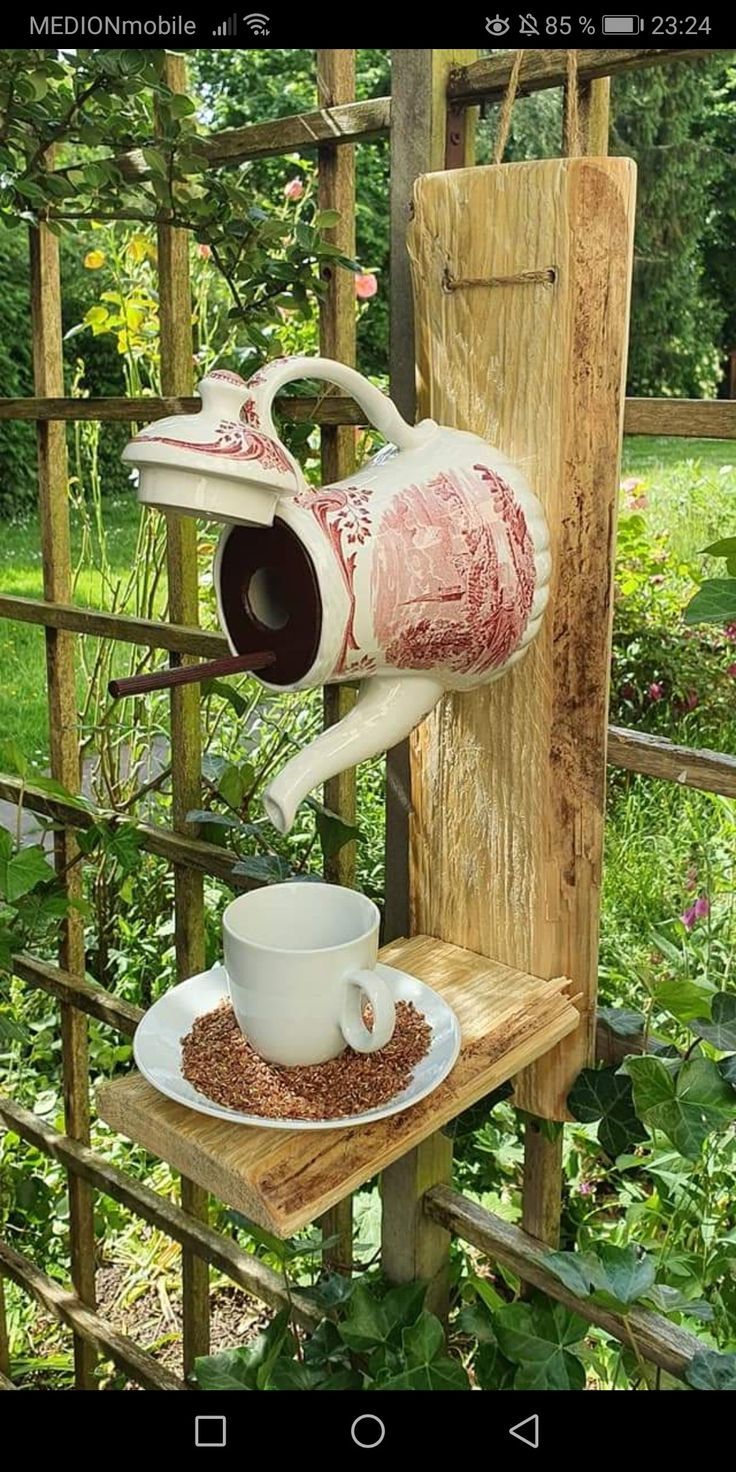 a bird feeder with a cup and saucer sitting on top of it next to a wooden fence