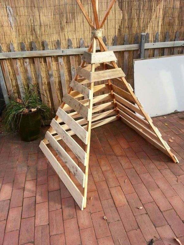 a wooden structure made out of pallet wood on the ground next to a fence