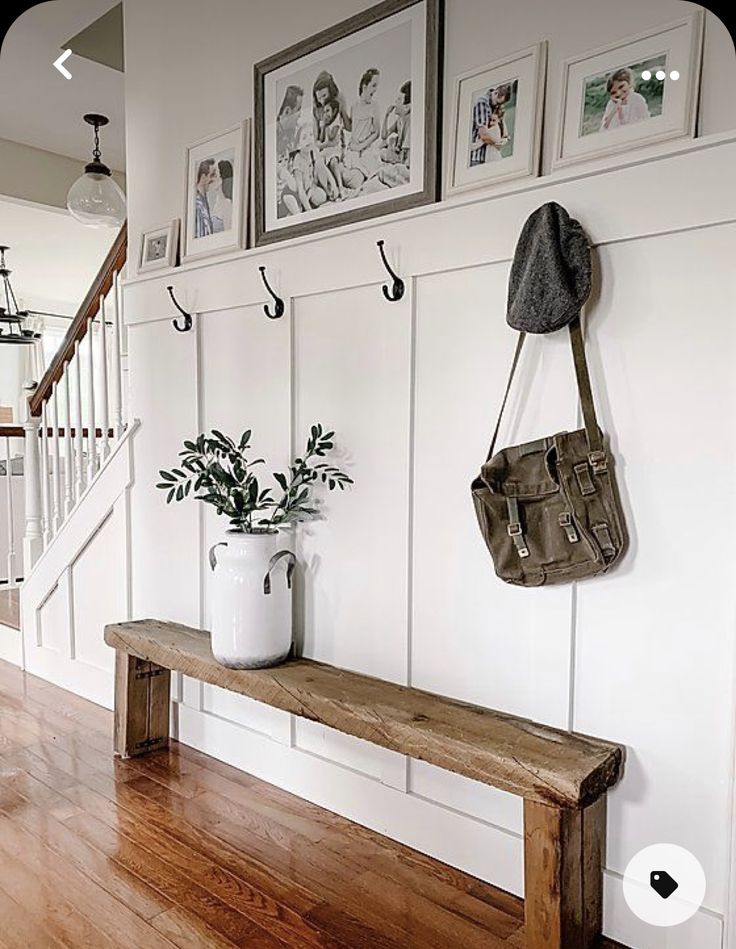 a wooden bench sitting in front of a white wall with pictures on the wall above it