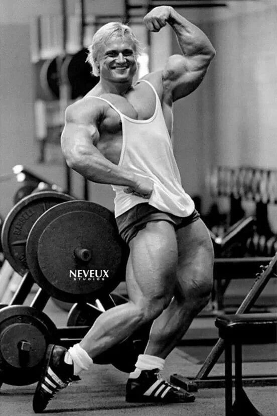 a man posing for the camera in front of a barbell