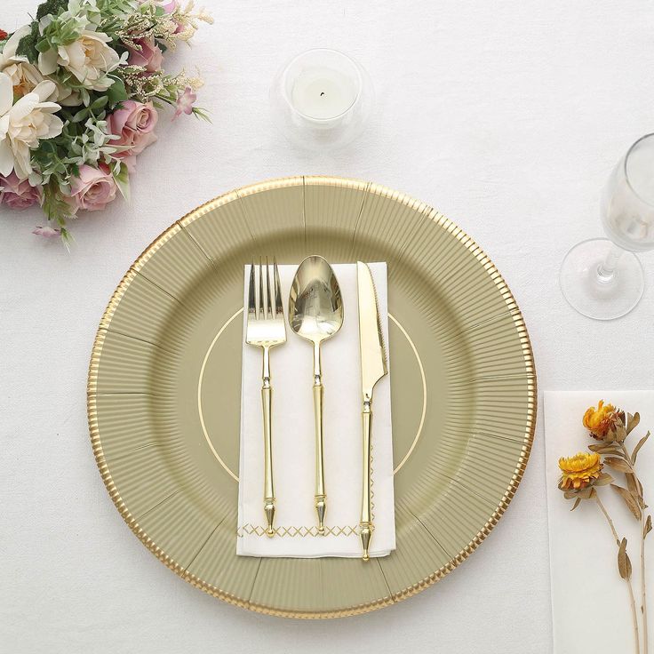 a white table topped with gold plates and silverware next to flowers on top of a wooden table