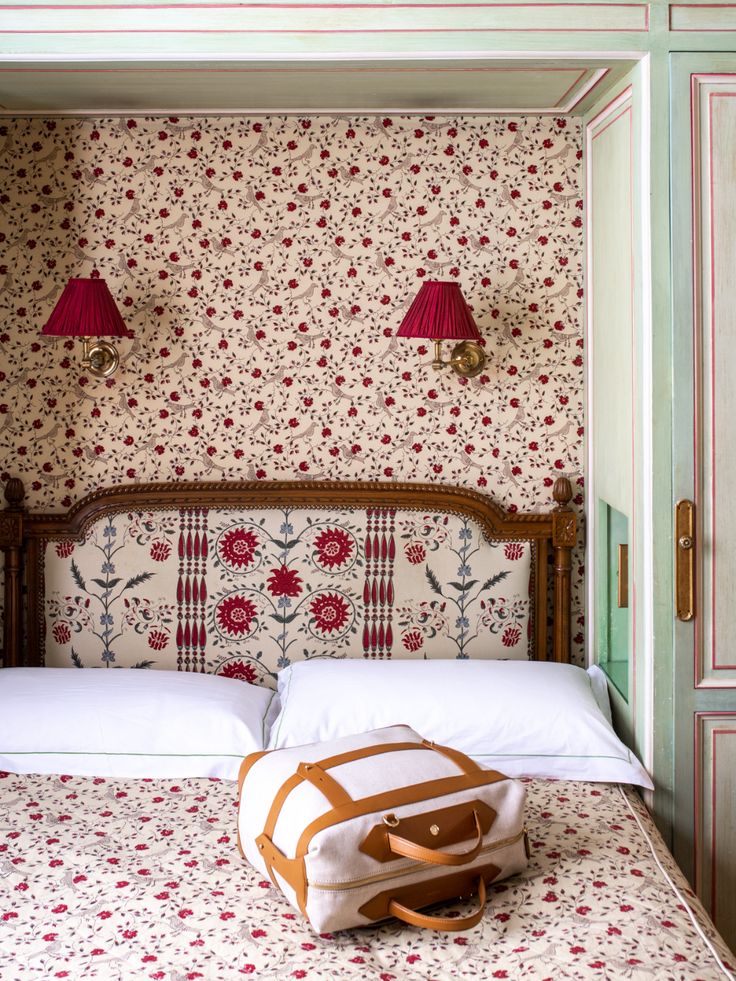 a bag sitting on top of a bed in a room with floral wallpaper and red lamps