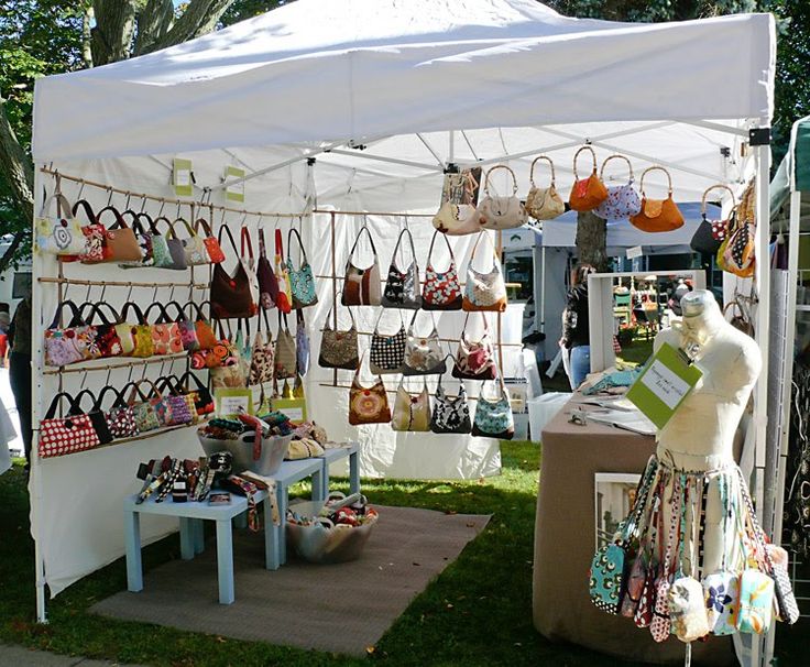 an outdoor market with handbags and purses hanging from the ceiling, in front of a white tent