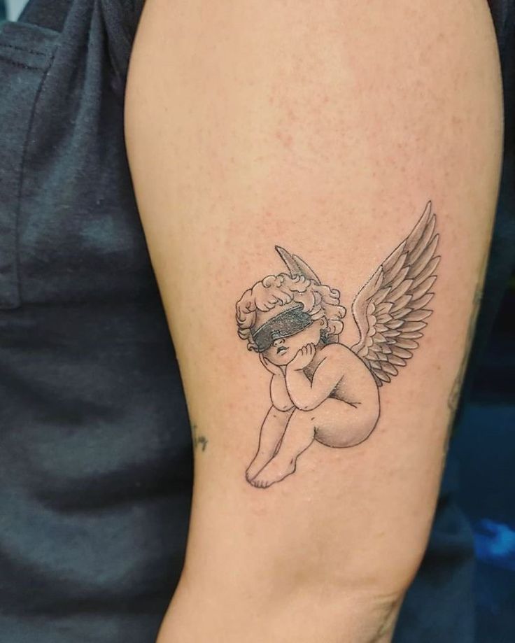 a small tattoo on the arm of a woman with an angel sitting on her knees