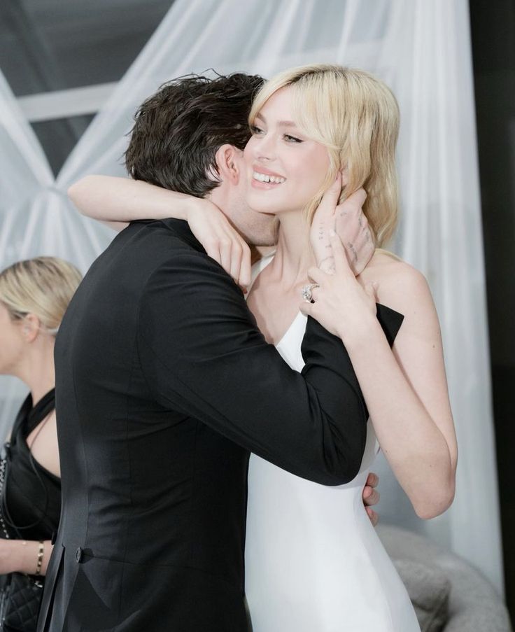 a man and woman hugging each other while standing in front of a white curtained wall