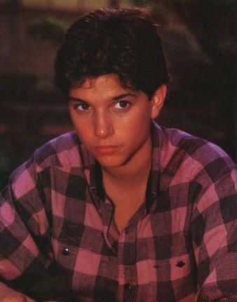 a young man sitting at a table with his hand on the keyboard and looking into the camera