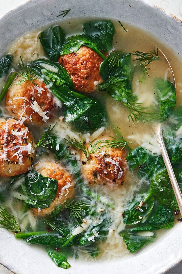 a bowl filled with meatballs and spinach covered in white sauce, garnished with parmesan cheese