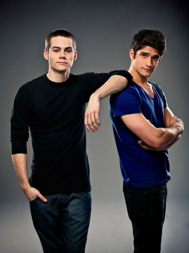 two men standing next to each other in front of a gray background with their arms crossed