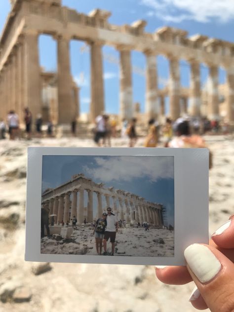 a person holding up a polaroid photo in front of the parthenion temple