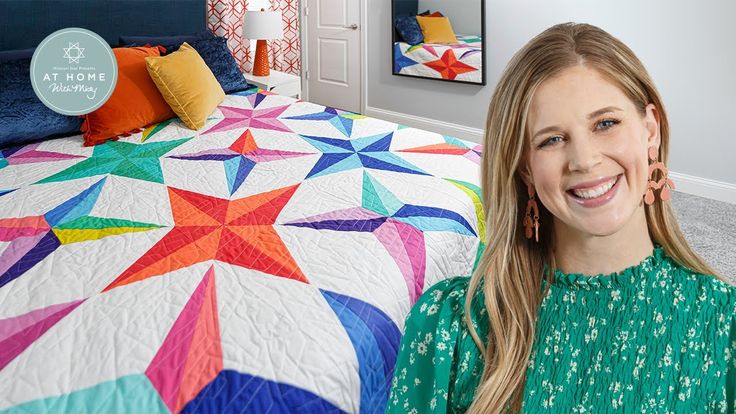 a woman standing in front of a bed with a colorful quilt on top of it