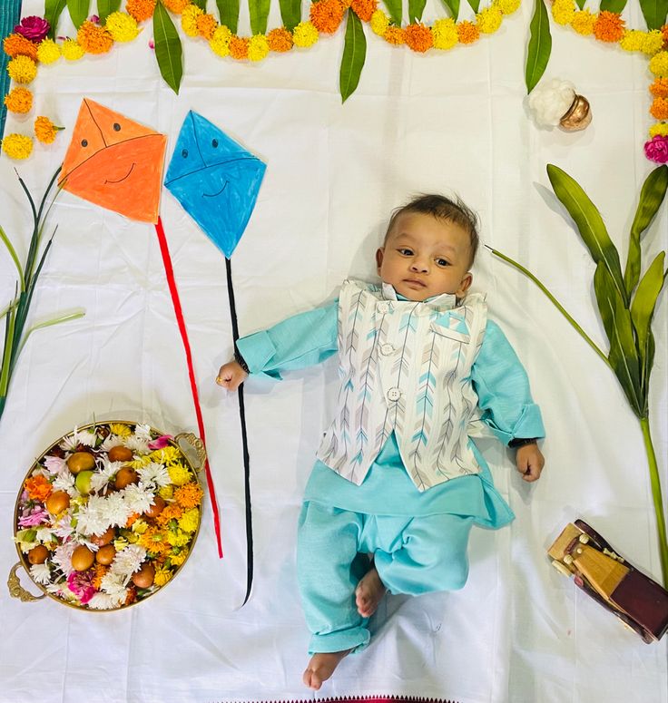 a baby is laying on the ground with flowers and kites in front of him