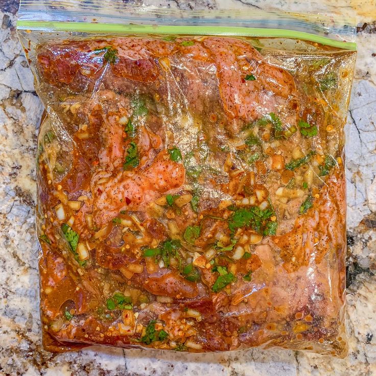 a plastic bag filled with meat and vegetables on top of a marble countertop next to a knife