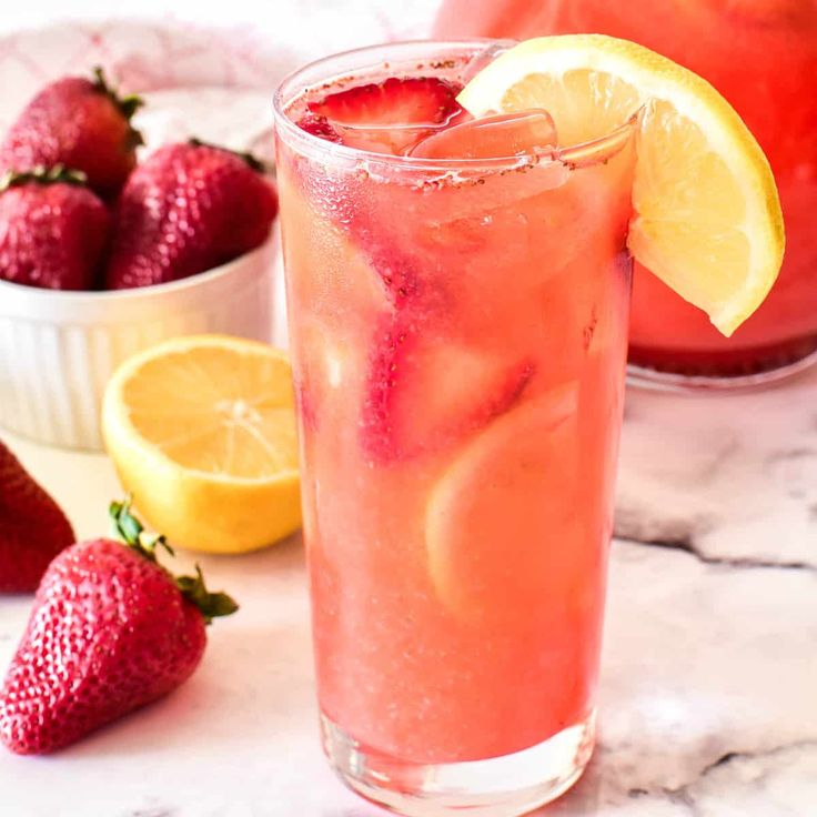 two glasses filled with watermelon lemonade next to strawberries and lemons