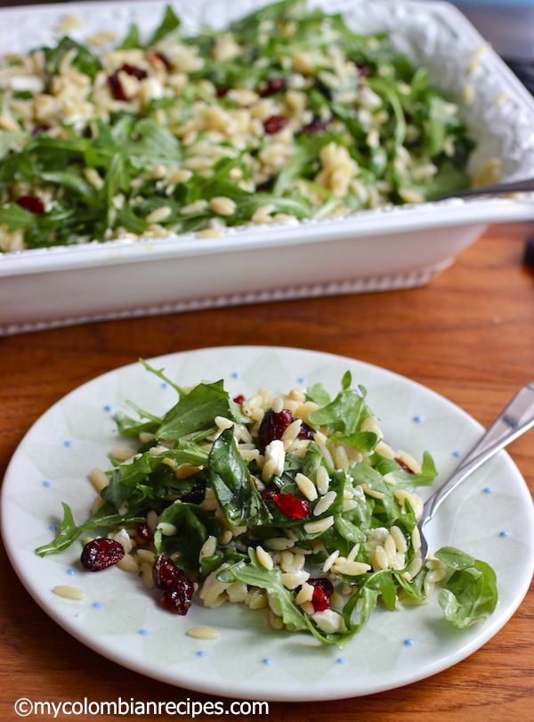 a white plate topped with salad next to a pan filled with greens and cranberries