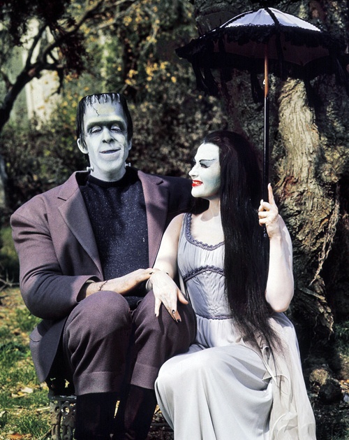 a man and woman dressed up as dracula and the corpse bride sitting under an umbrella