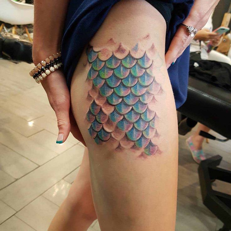 a woman is showing off her colorful fish scale tattoo on her thigh and leg,