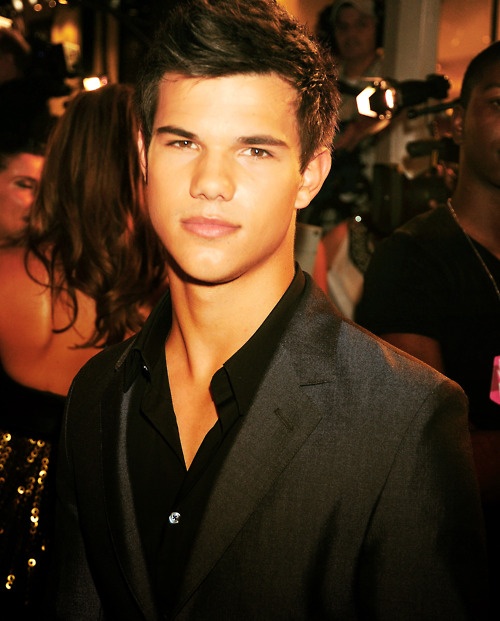 a young man in a suit and black shirt posing for the camera at an event