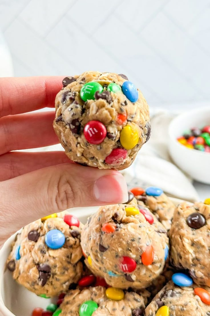 a hand holding a cookie ball over a bowl full of m & m cereal balls