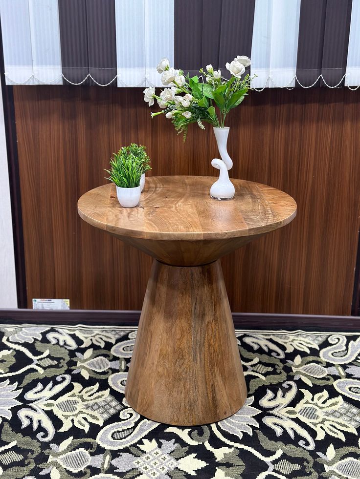 two white vases with flowers sit on top of a wooden table in front of a wall