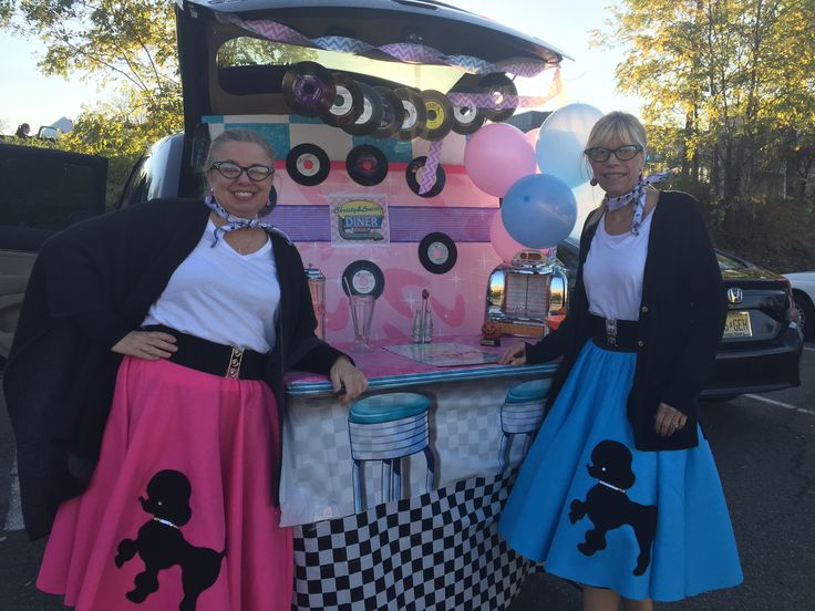 two women dressed in costumes standing next to a food truck with balloons on the back