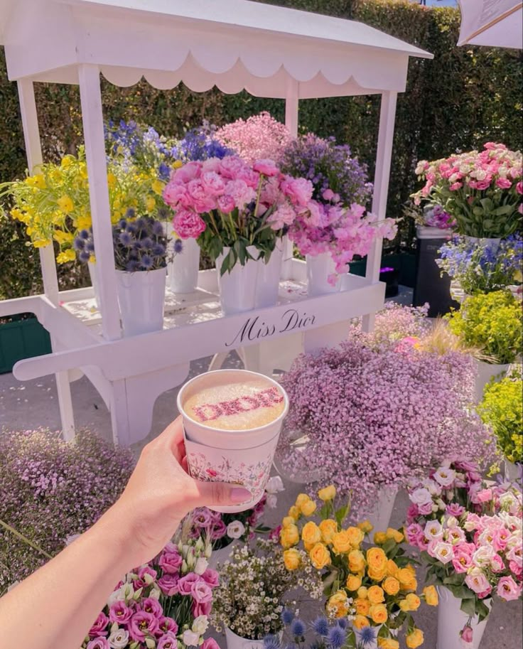 a person holding up a cup in front of flowers on display at a flower shop