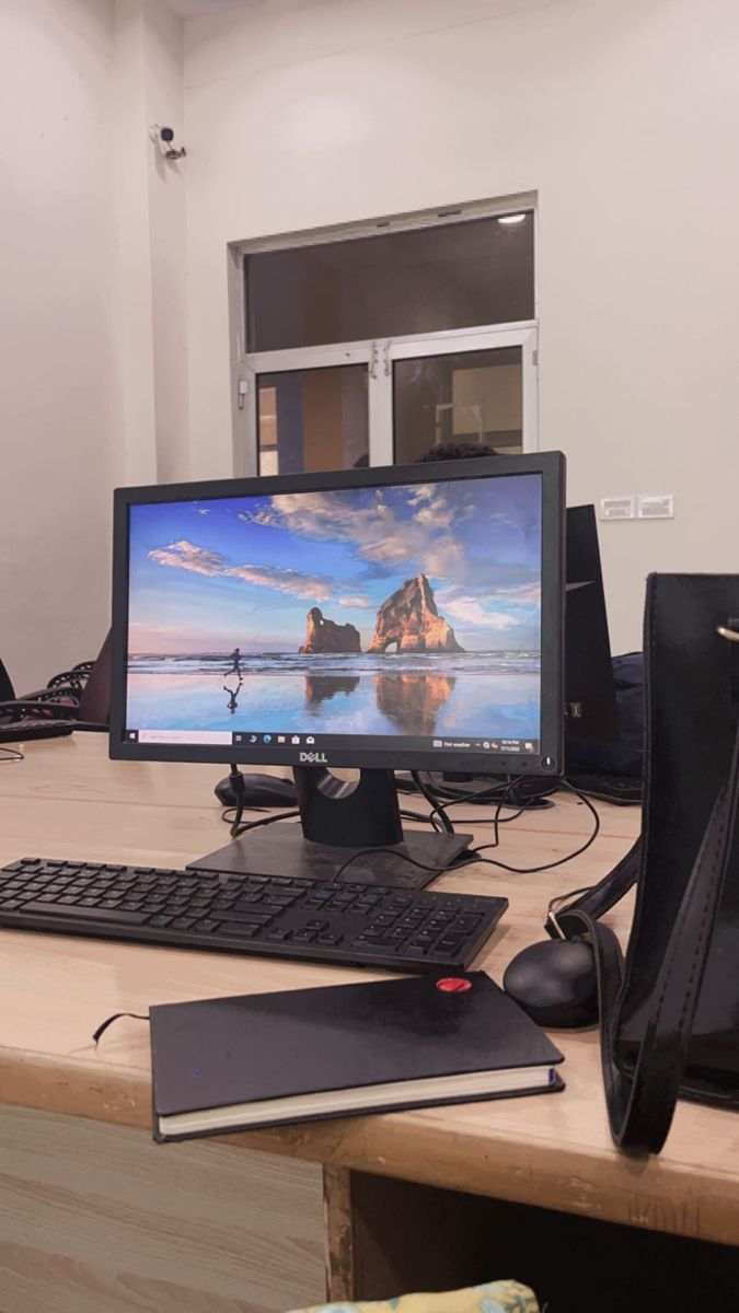 a desktop computer sitting on top of a wooden desk next to a black bag and keyboard