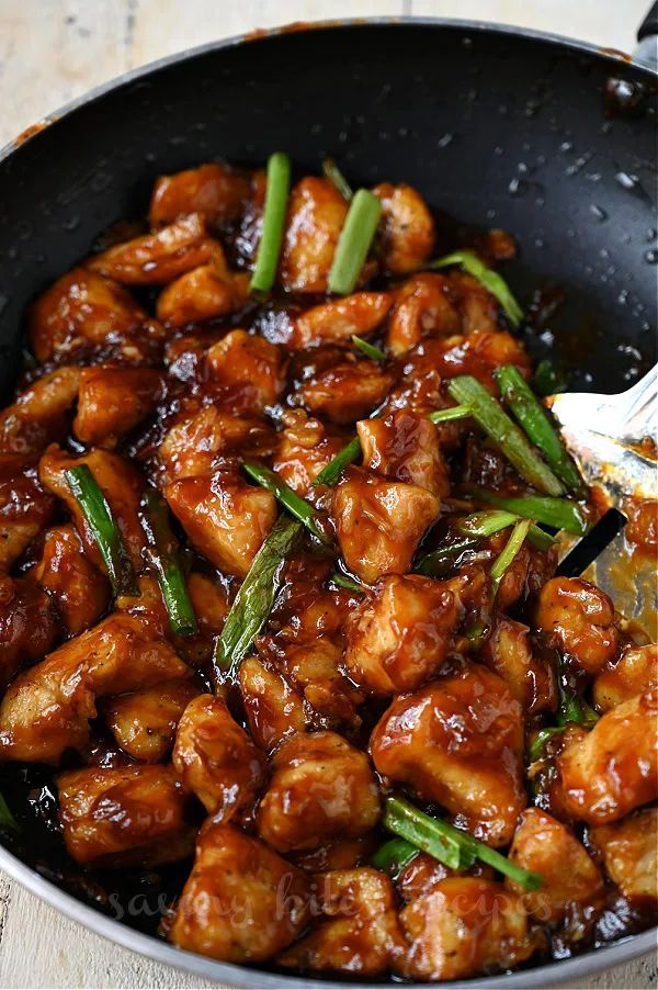 a pan filled with chicken and green beans on top of a wooden table next to a fork