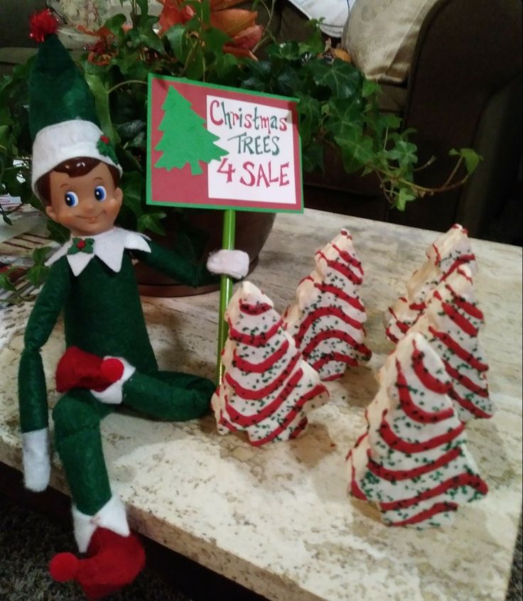 an elf is sitting on a table with christmas trees for sale