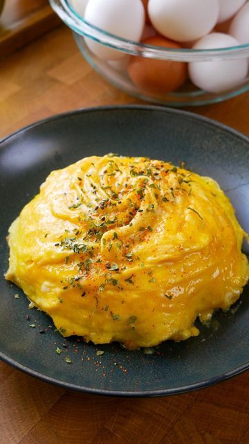 an omelet on a black plate next to some eggs in a glass bowl