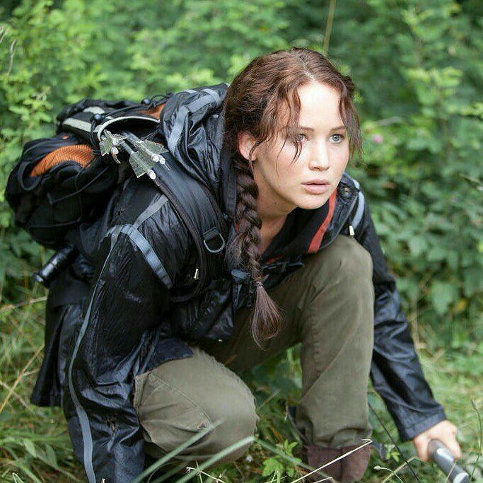 a woman crouching down in the grass with a backpack on her back, looking at the camera