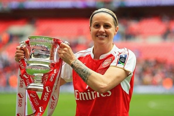 a woman holding up a trophy on top of a soccer field with fans in the stands