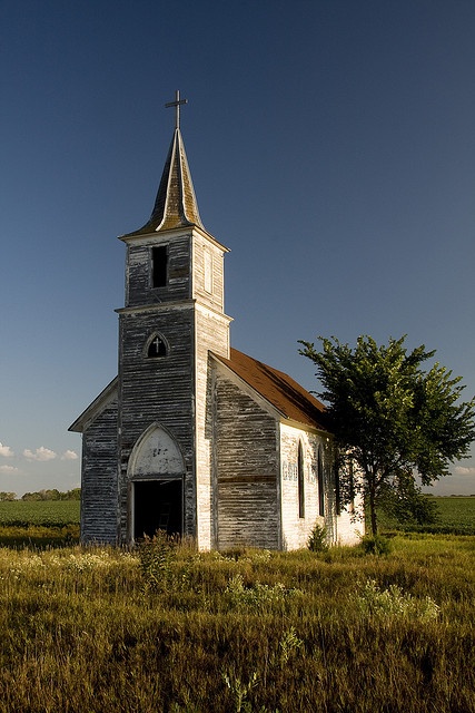 an old wooden church with a steeple in the middle of a grassy field under a blue sky