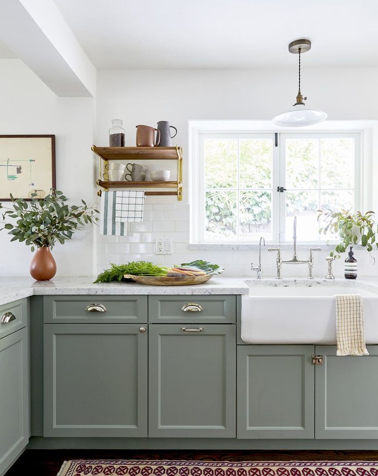 a kitchen with green cabinets and white counter tops is pictured in this image, there are two potted plants on the window sill above the sink