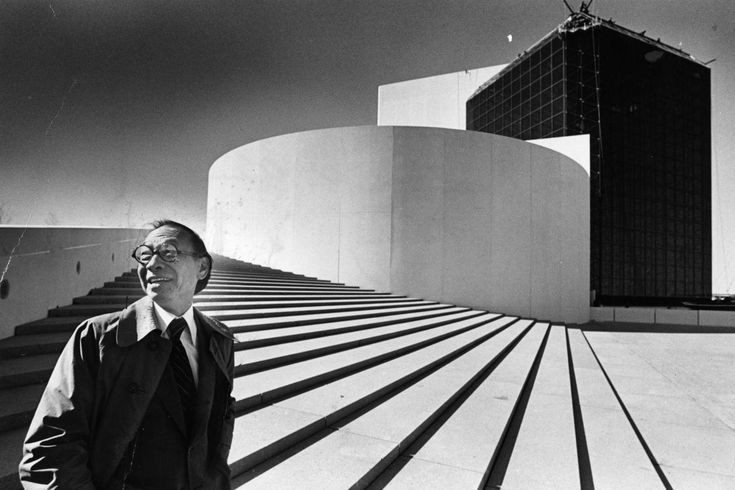 a man wearing glasses standing in front of a building with stairs leading up to it