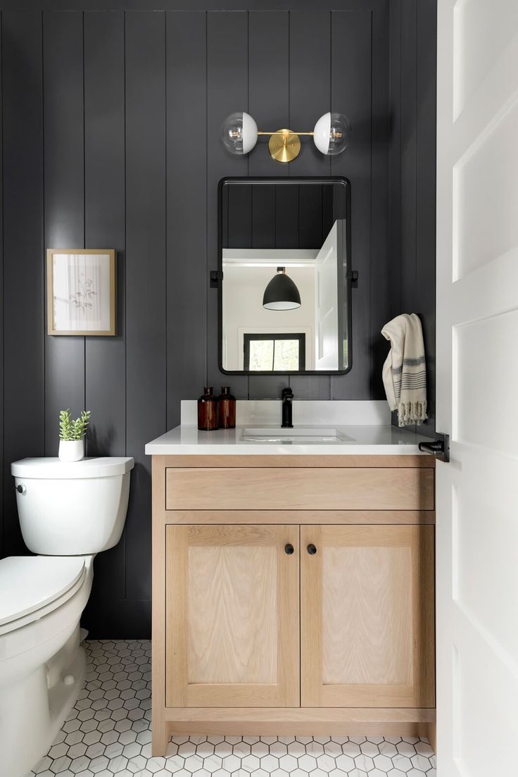 a white toilet sitting next to a bathroom sink under a mirror on top of a wooden cabinet