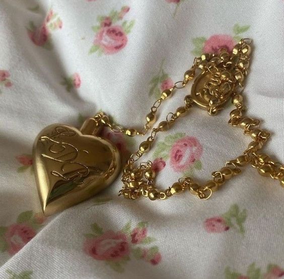 two gold necklaces sitting on top of a flowered cloth covered tablecloth with pink roses