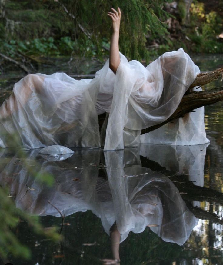 a woman in a white dress is floating on the water with her arms outstretched up