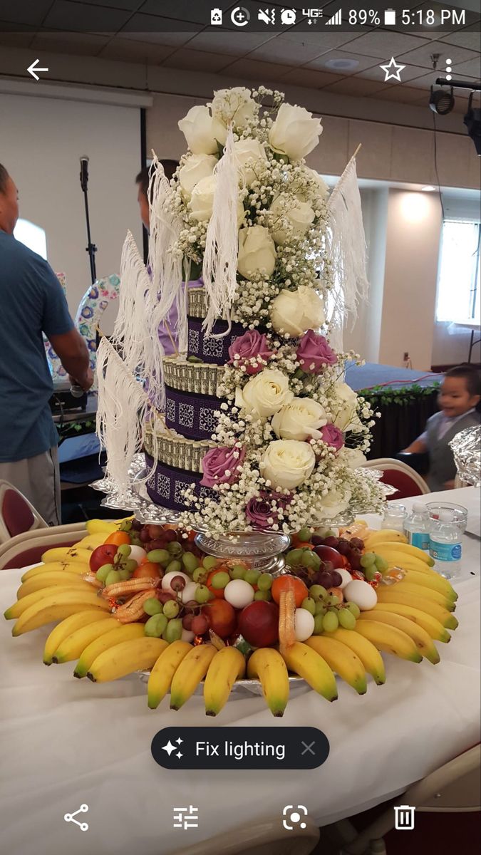 a table topped with a tall cake covered in fruit and flowers next to a crowd of people