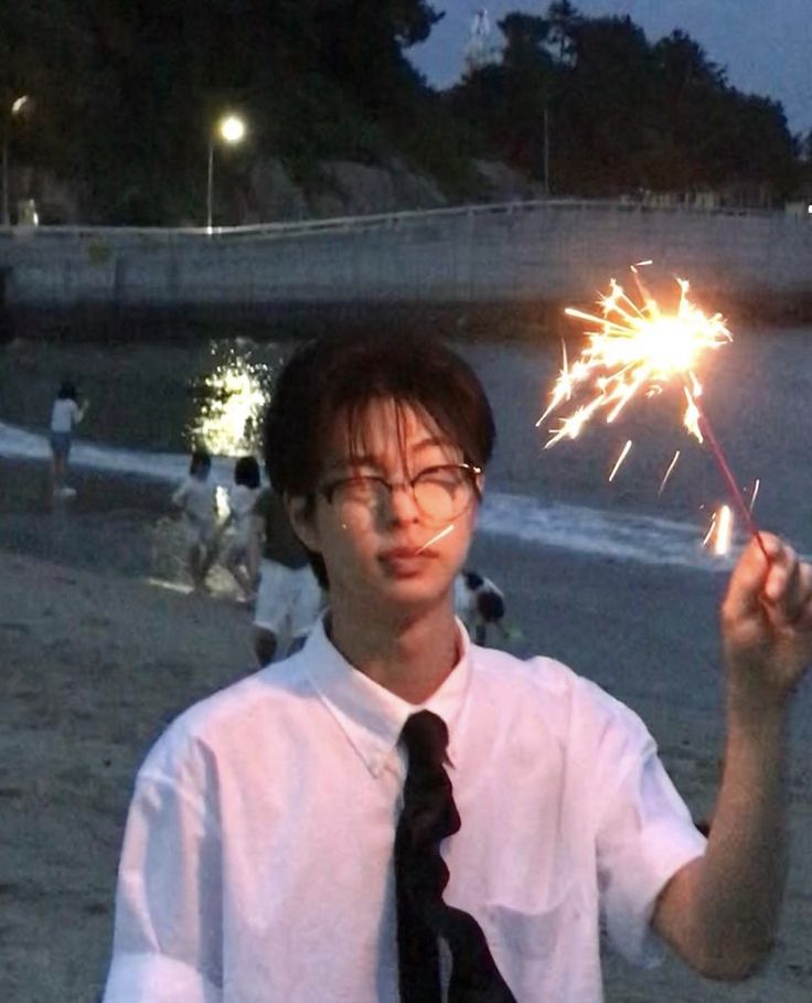 a man in glasses and tie holding up a sparkler on the beach at night