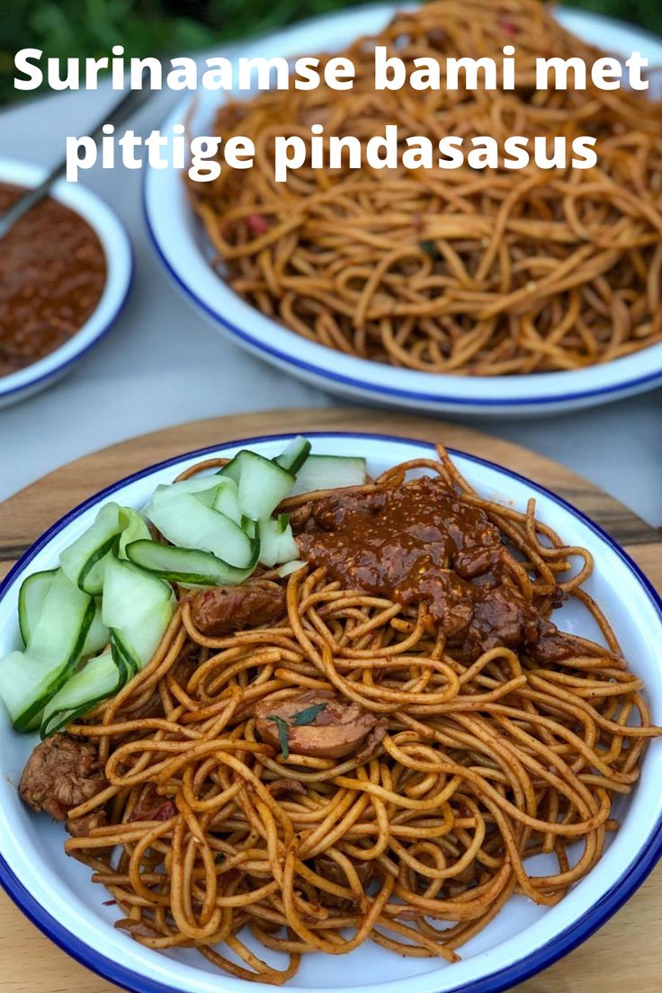 two plates filled with noodles and meat on top of a wooden table next to sauce