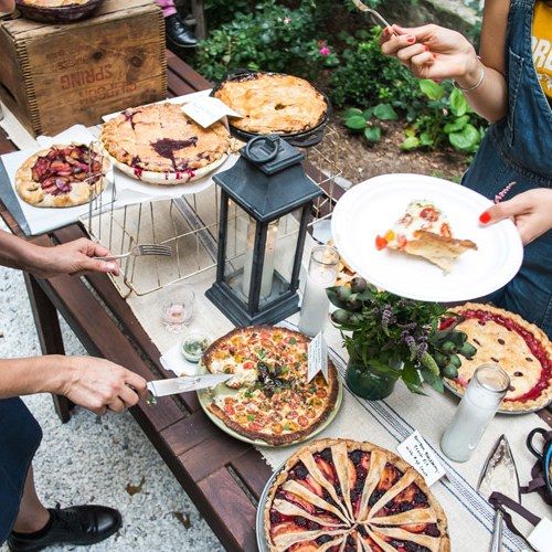 several people sitting at a table with many pies on it