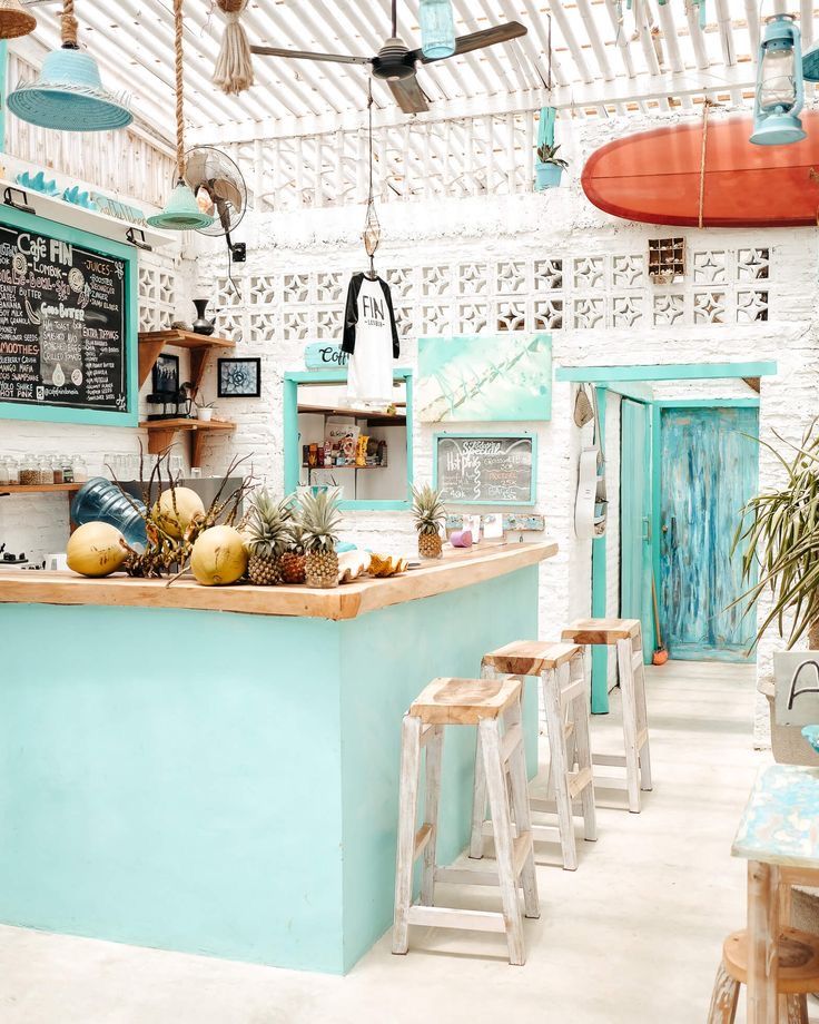 a blue and white restaurant with surfboards hanging from the ceiling, two stools at the bar