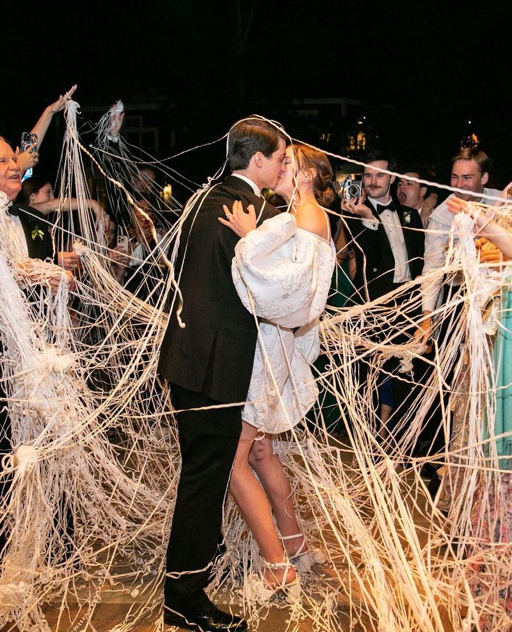 a bride and groom kissing in front of their wedding party with streamers on the dance floor