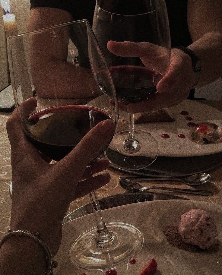 two people are toasting with red wine in front of each other at a dinner table